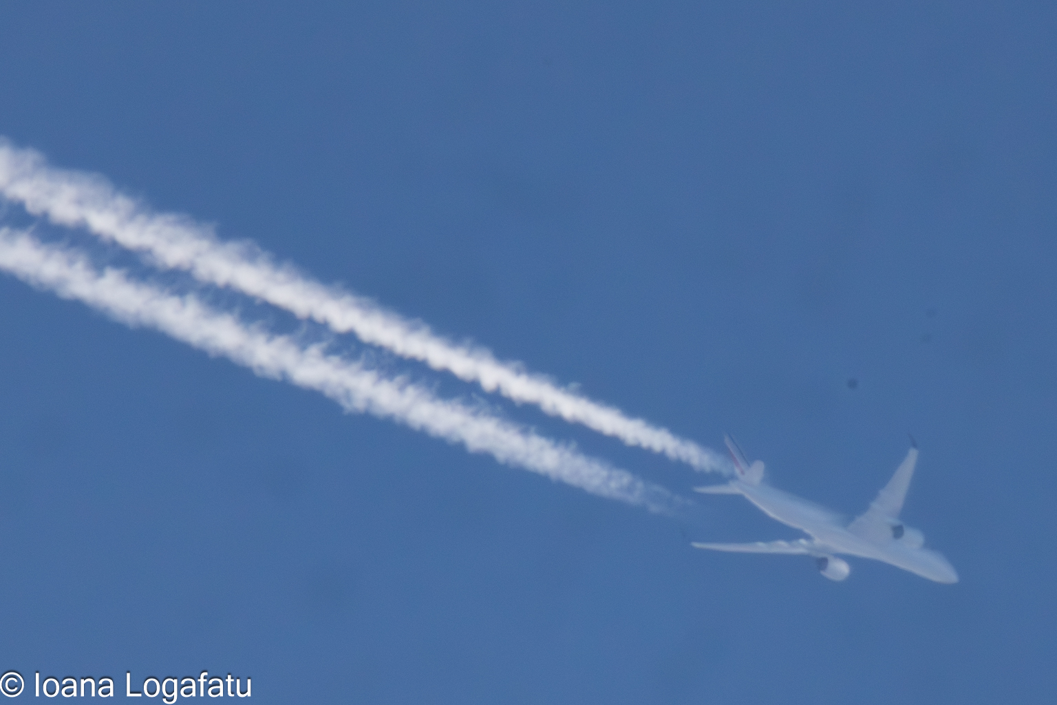High above the clouds, an airplane leaves trails